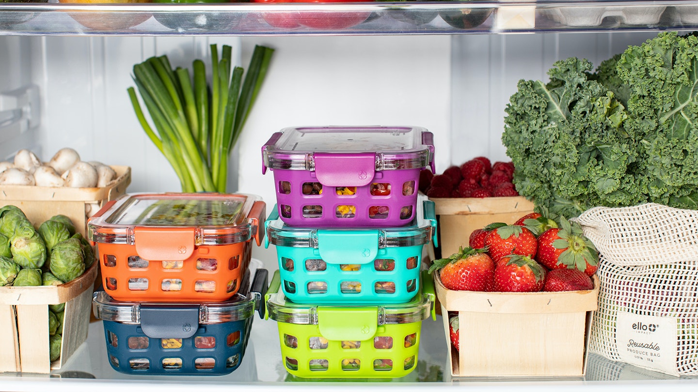 Colourful containers stacked amongst veggies on a refrigerator shelf