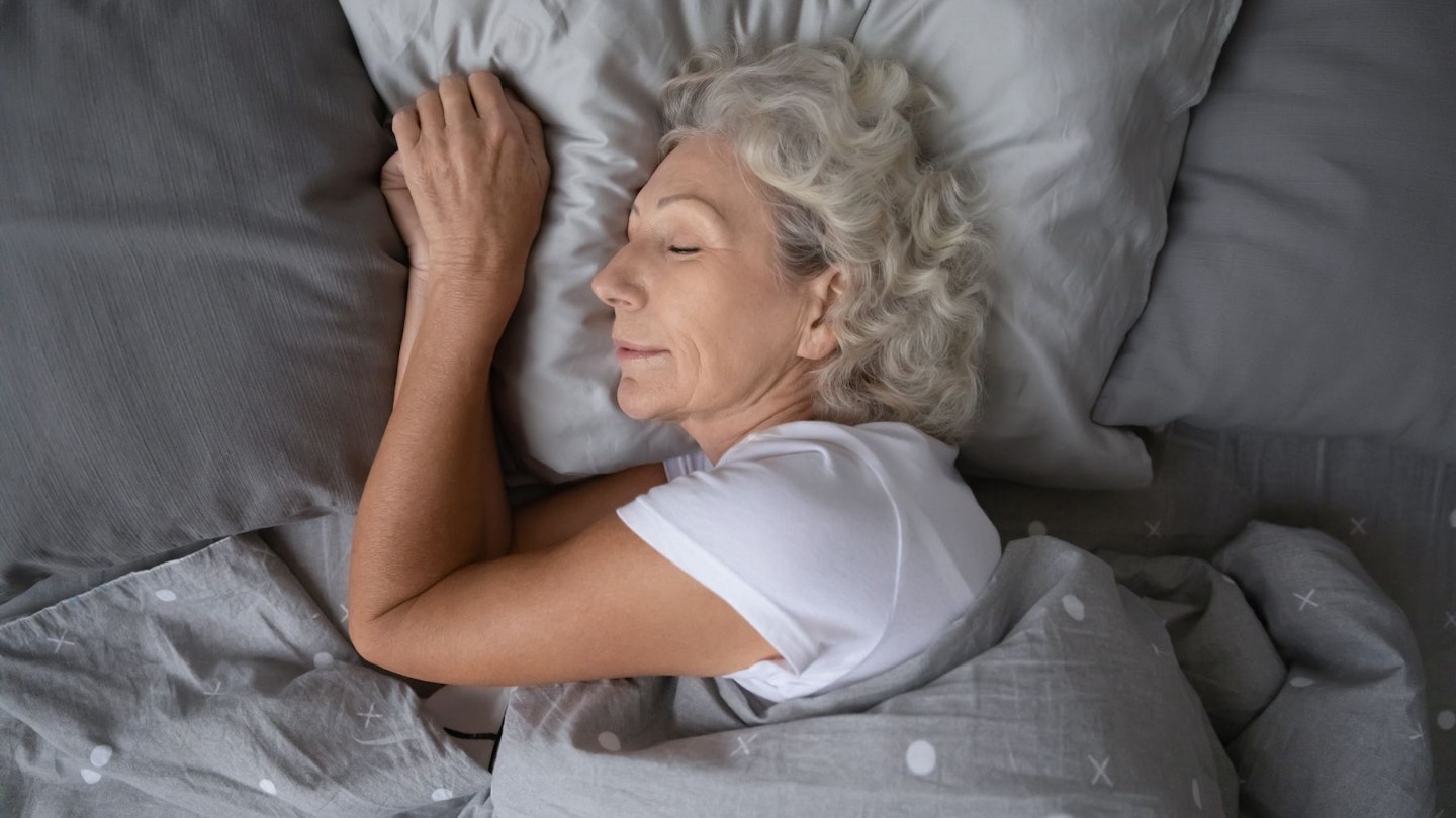 Body pillow: senior woman sleeping on grey bed