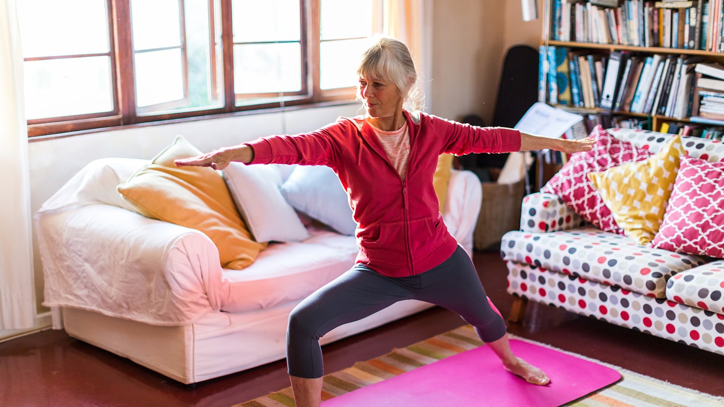 Older woman exercising at home on a pink yoga mat 
