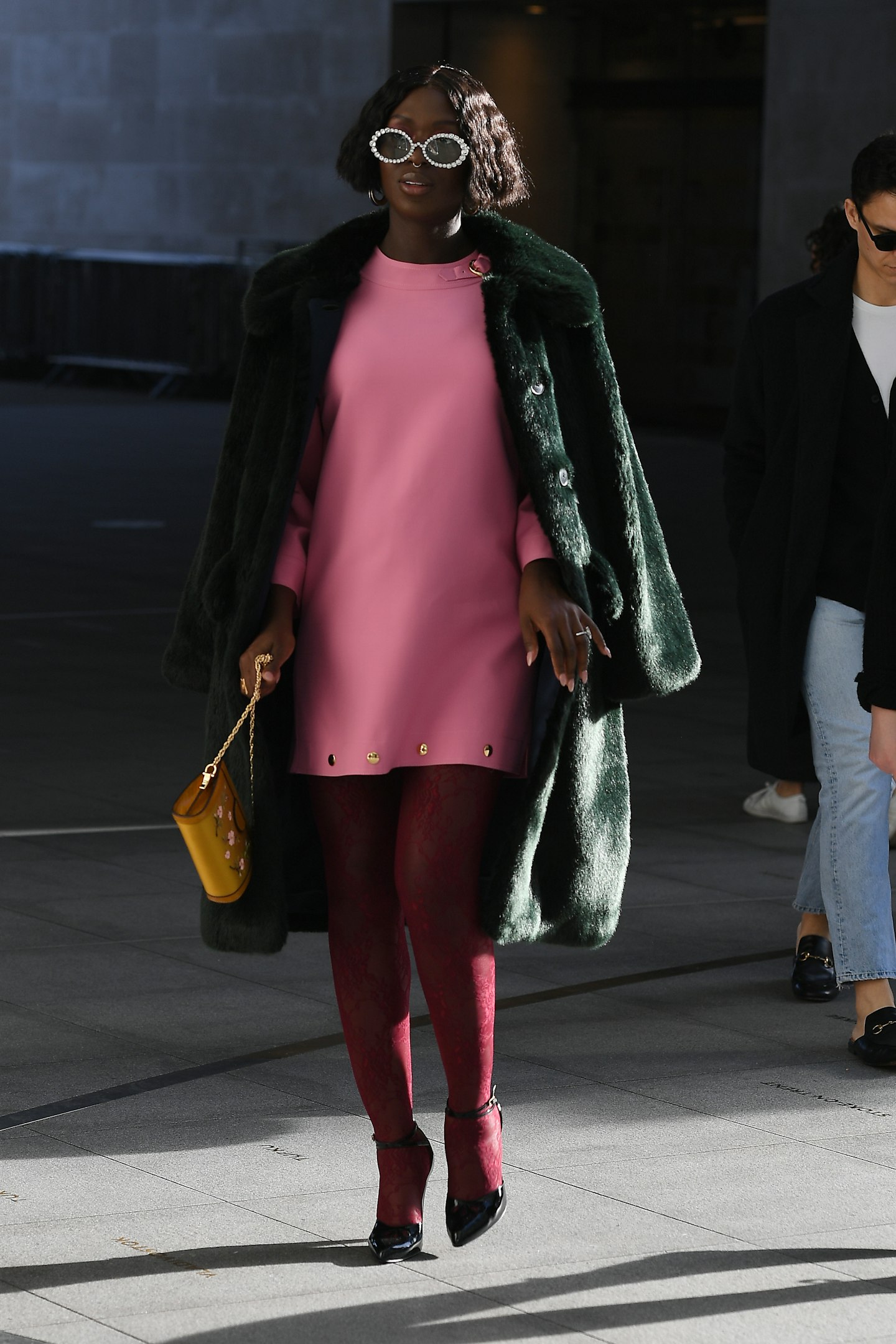 Jodie Turner-Smith wearing a pink dress and faux-fur green coat 