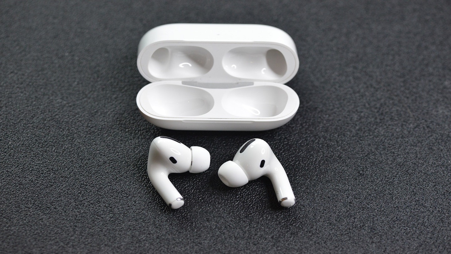 A white pair of Airpods lying on a flat surface next to a white Airpods case.