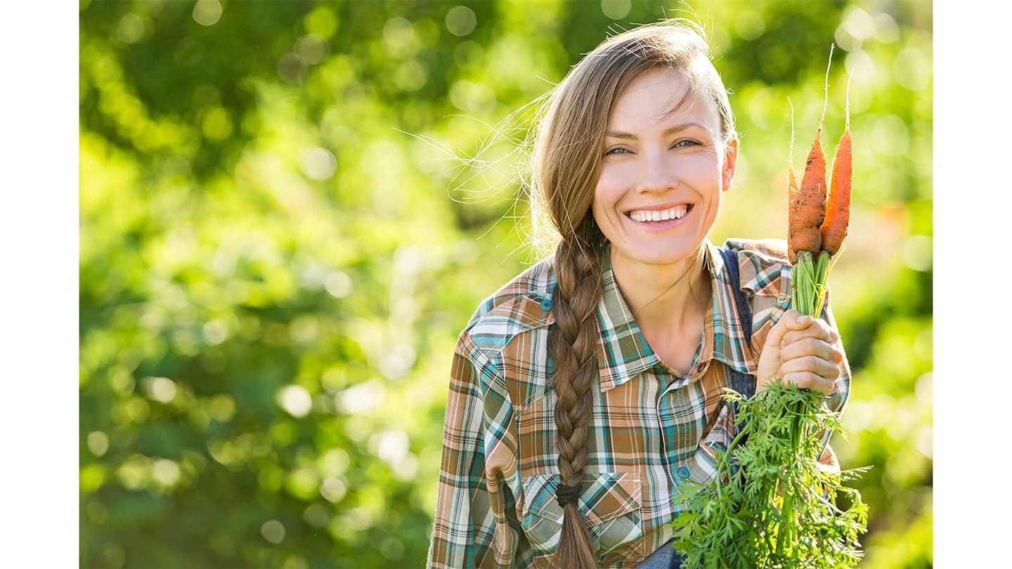 woman with long hair holding up bunch of freshly picked carrots