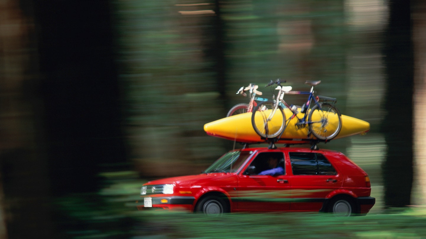 A red VW Golf with a roof rack carrying bikes and a kayak