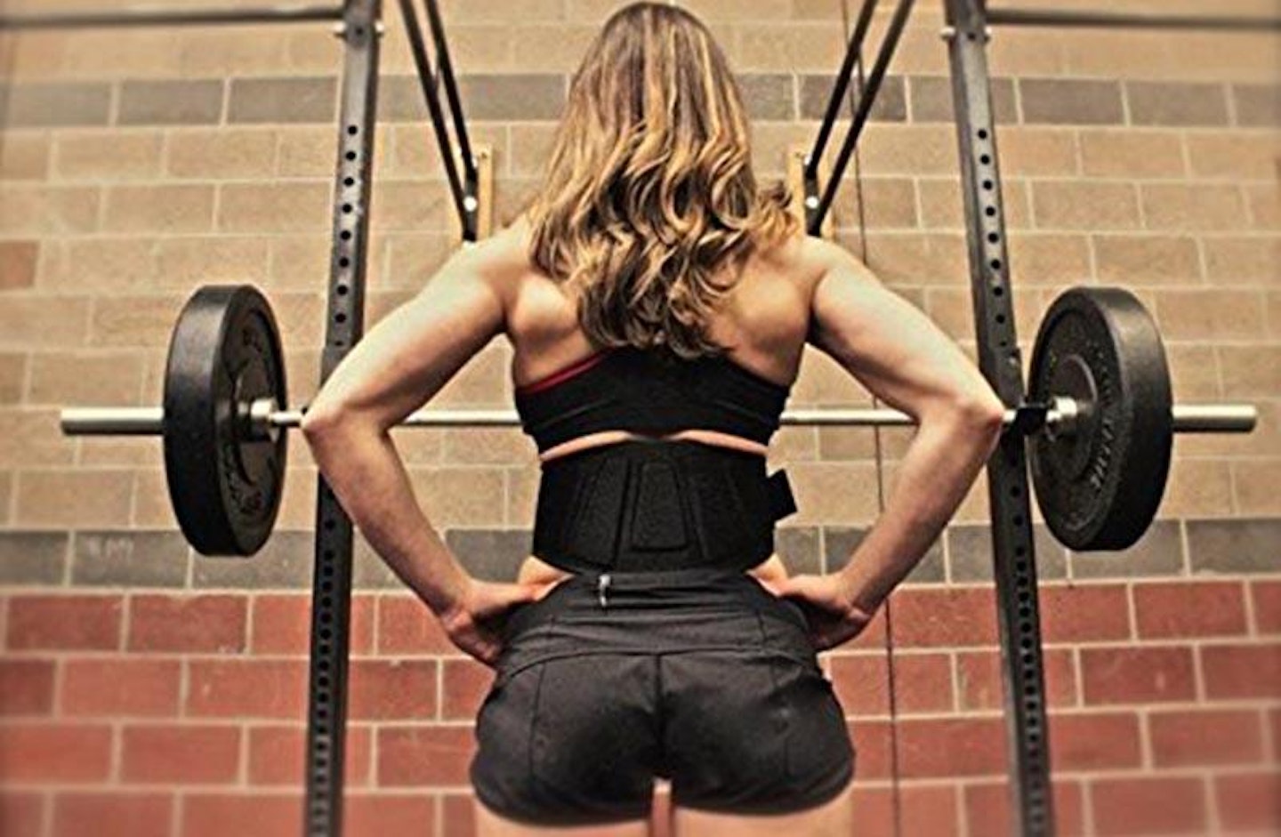 Woman standing at weight rack wearing weight belt