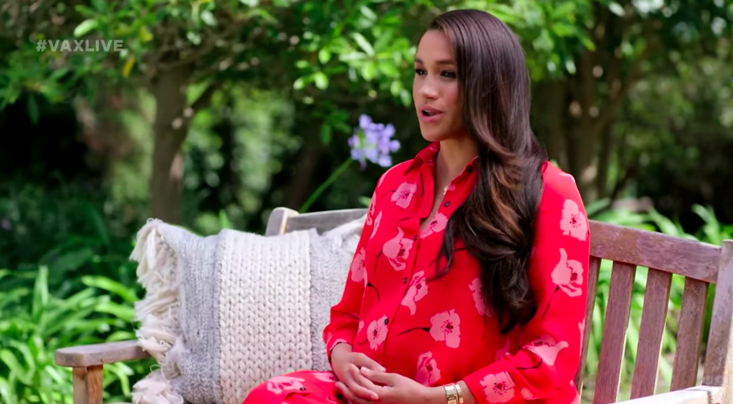 Meghan Markle sitting on a bench wearing a red dress from Carolina Herrera 