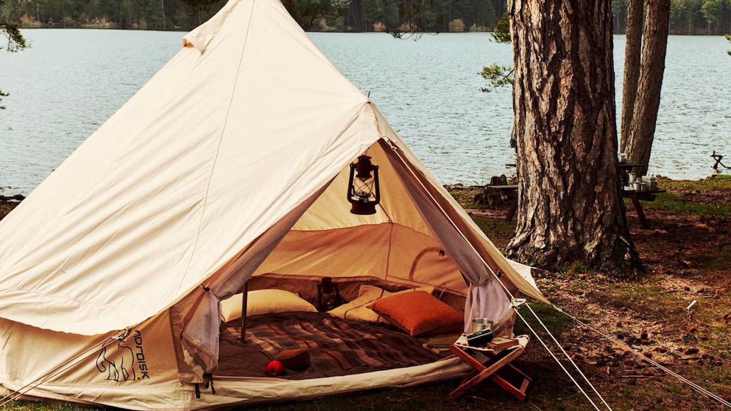 A Nordisk tent pitched by a lake with blankets and pillows inside 