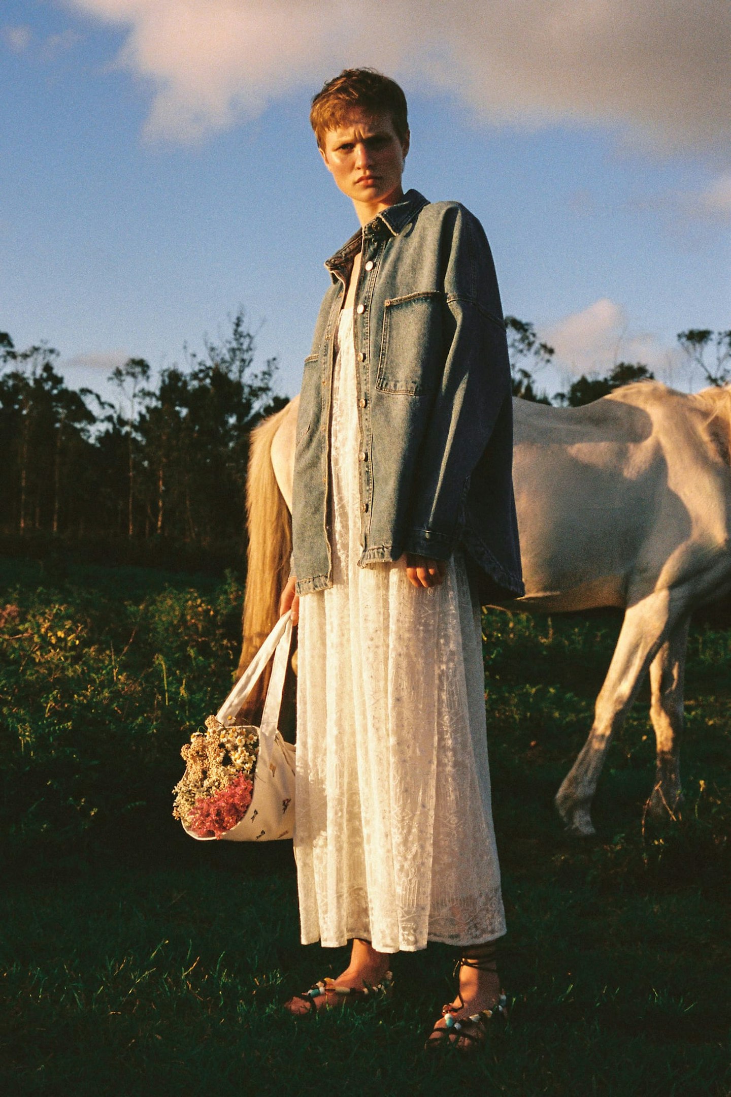 A model wearing a denim jacket and carrying a flower bag 
