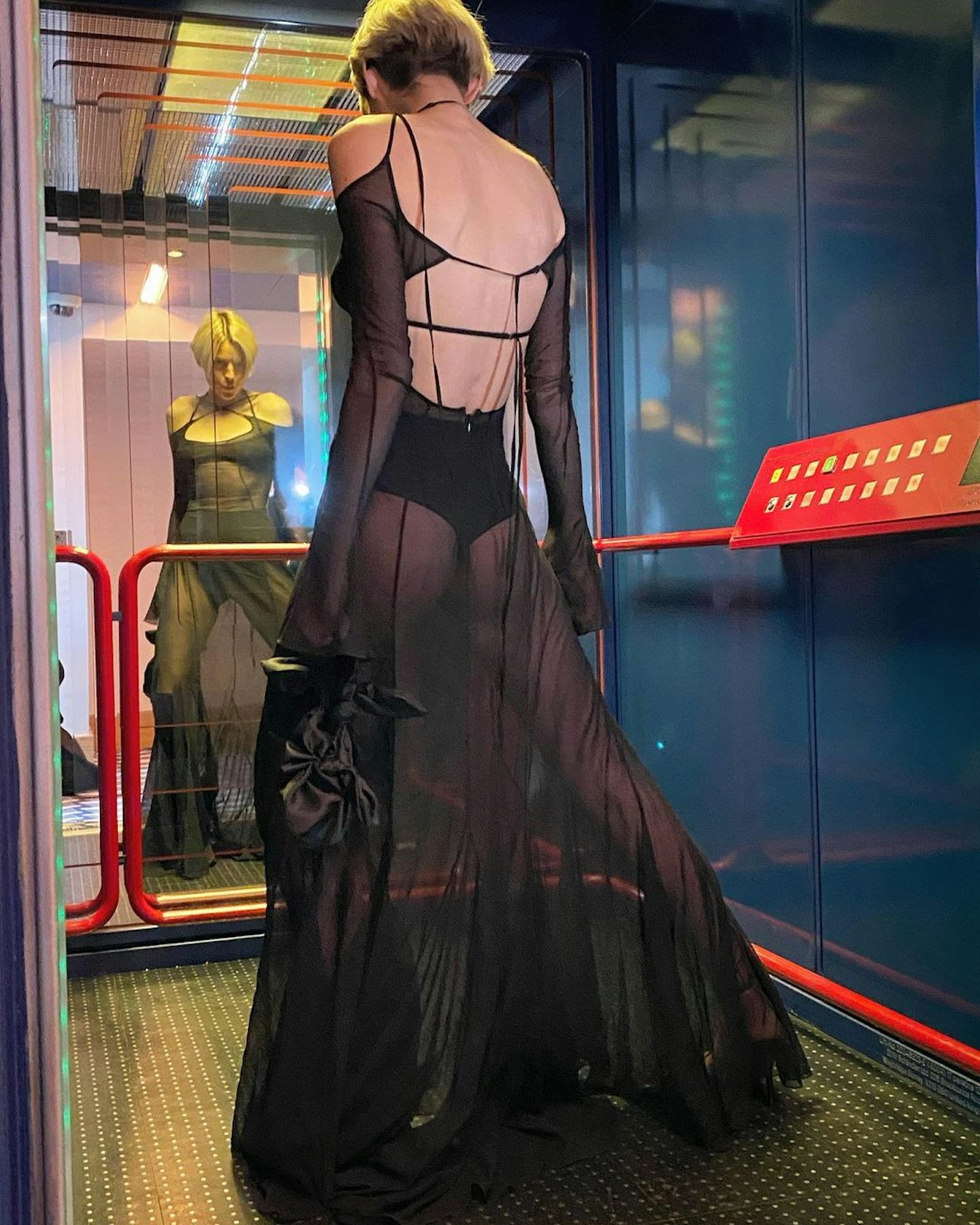 Emma Corrin standing in a lift wearing a sheer dress from Charlotte Knowles