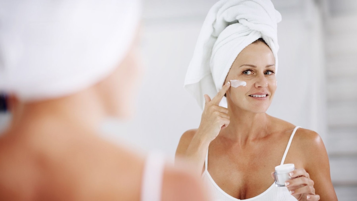 woman applying eye cream in mirror