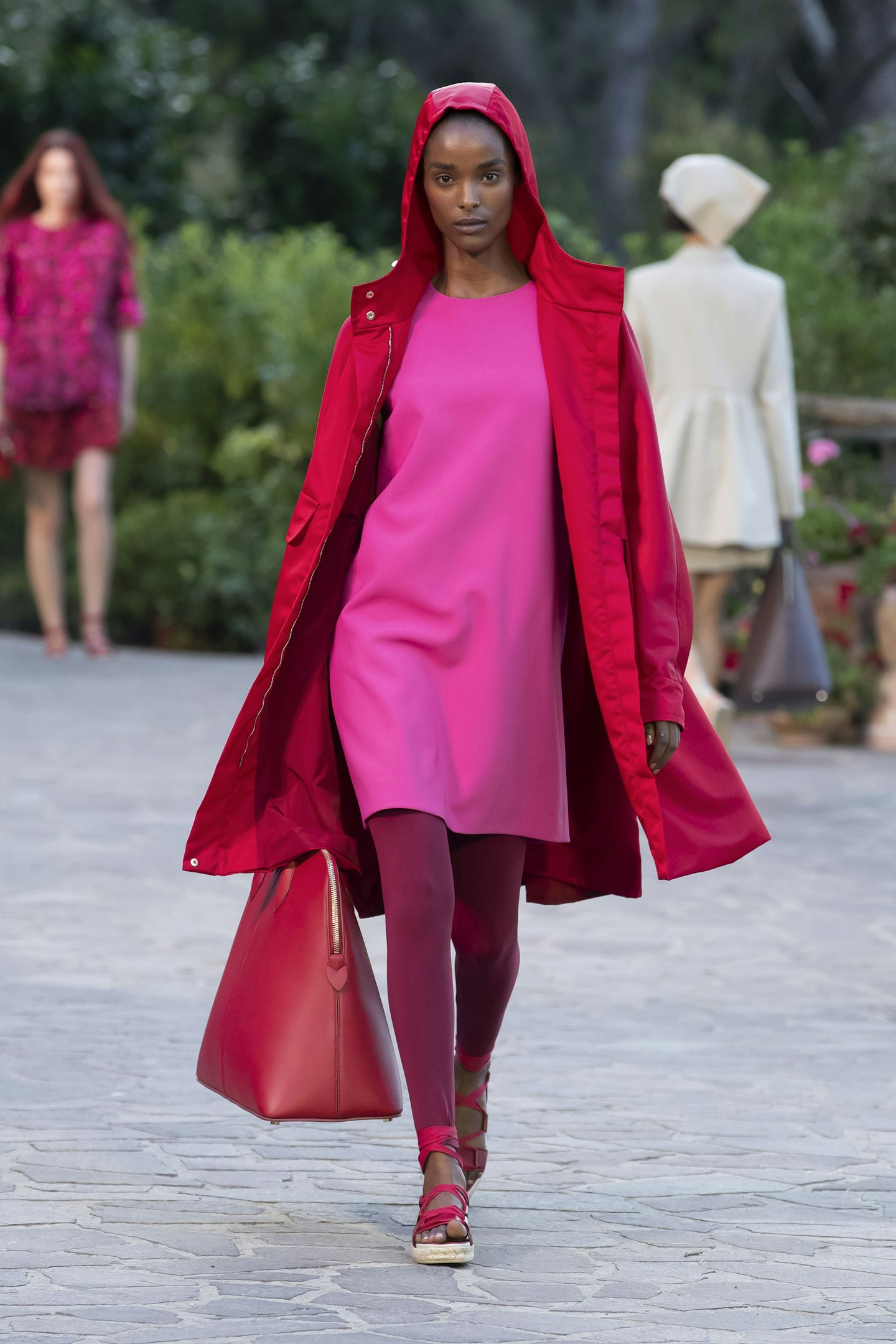 A model wearing a pink dress and red coat at Max Mara Resort 2022