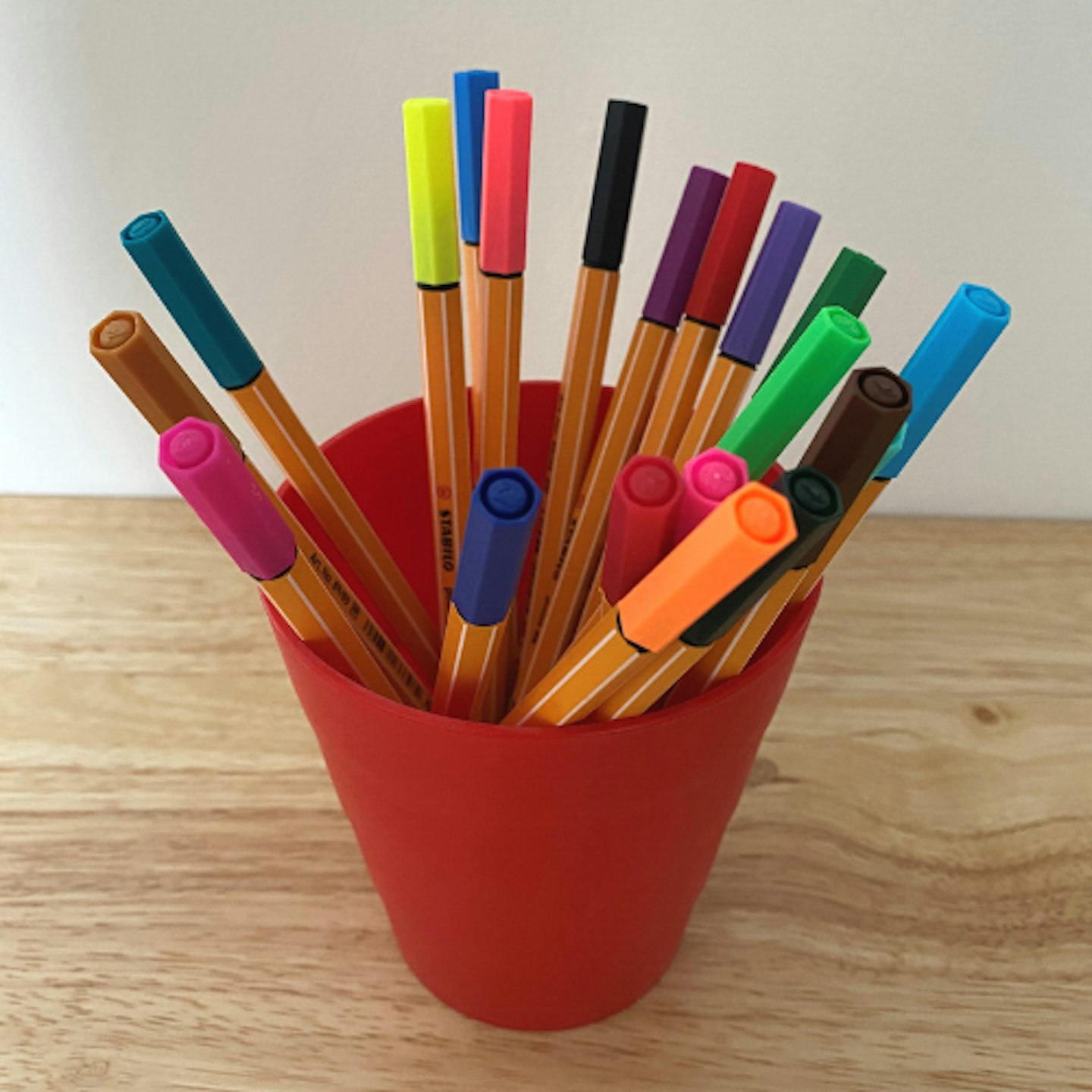 Multi-coloured pens in a red pot on a white background