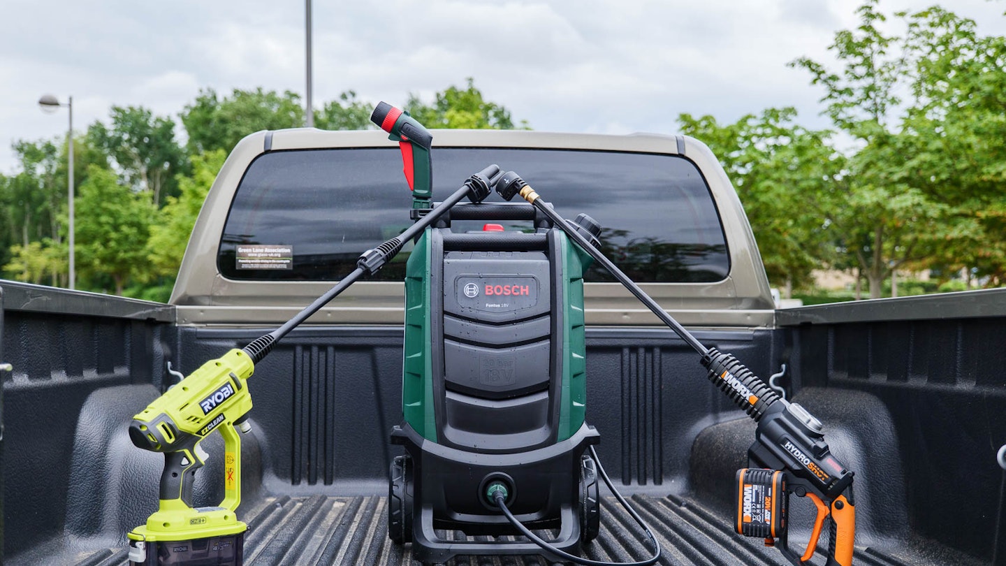 Ryobi RY18PW22A-125 18V ONE+ Cordless 22bar Power Washer, Bosch FONTUS Gen II 18v Cordless Low Pressure Washer 20 Bar and the WORX WG630E.1 18V (20V MAX) 4.0Ah Cordless Brushless Hydroshot Portable Pressure Cleaner in the bed of a pickup truck