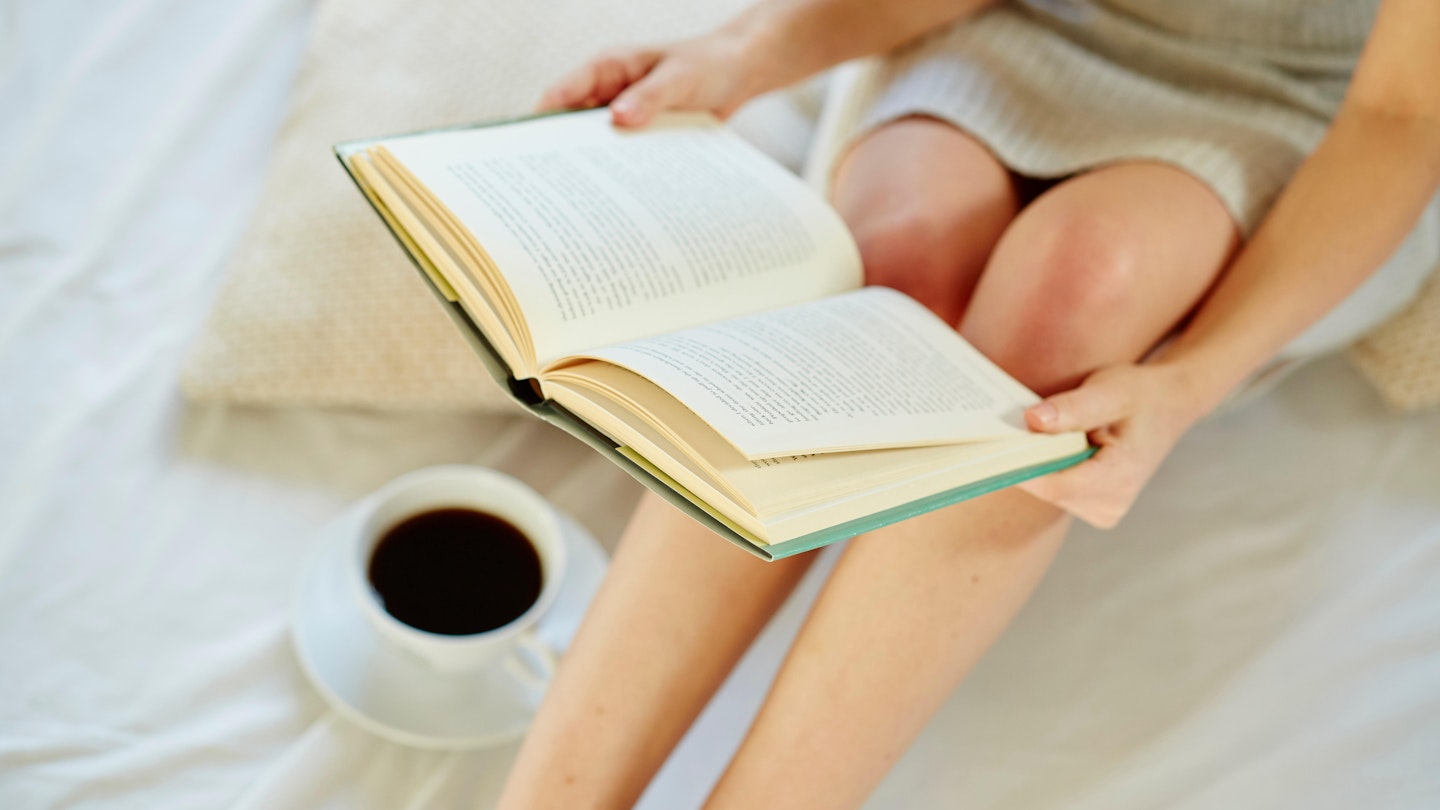 lady reading book on bed with coffee cup to her right
