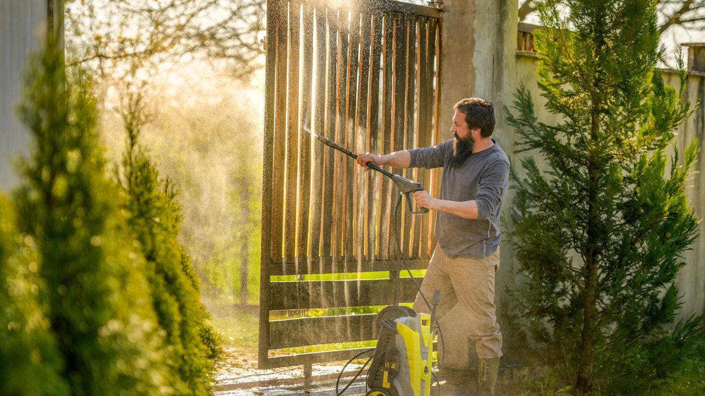 the best pressure washers - modern gardens - man pressure washing a gate