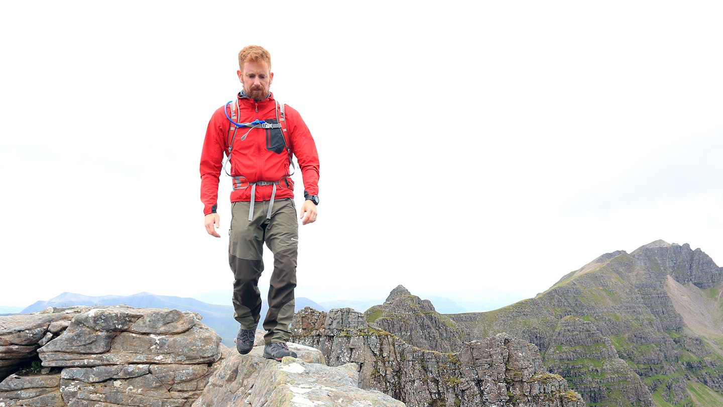 Hiker walking along ridgeline wearing softshell jacket and hiking trousers