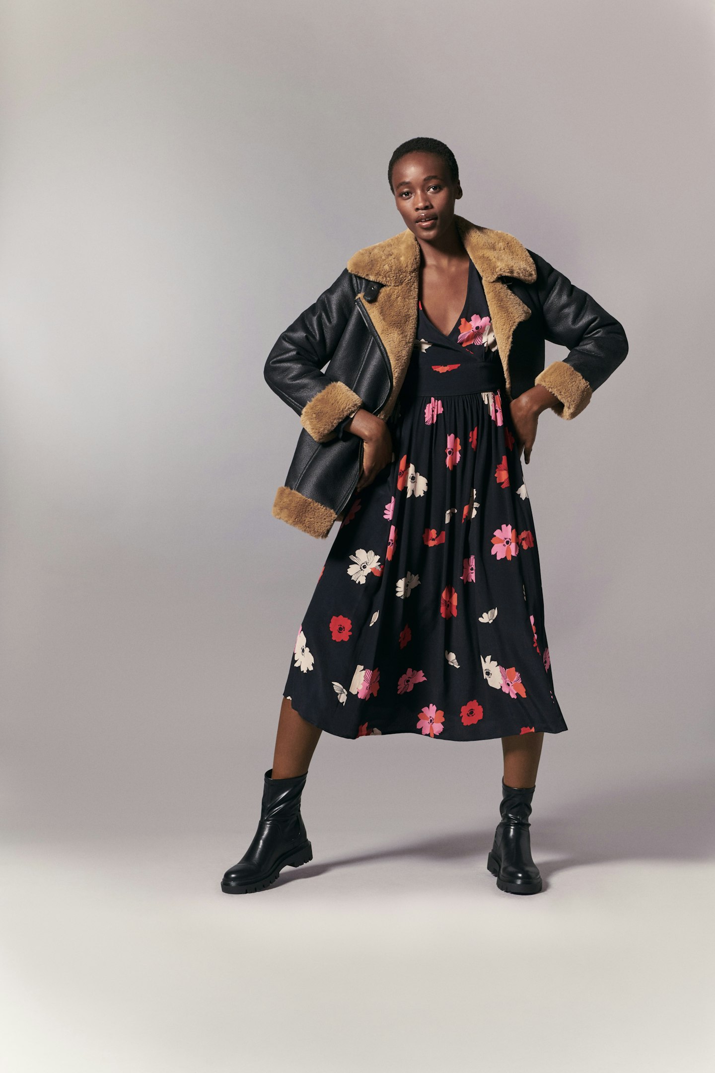 A model wearing a black floral dress with an aviator jacket
