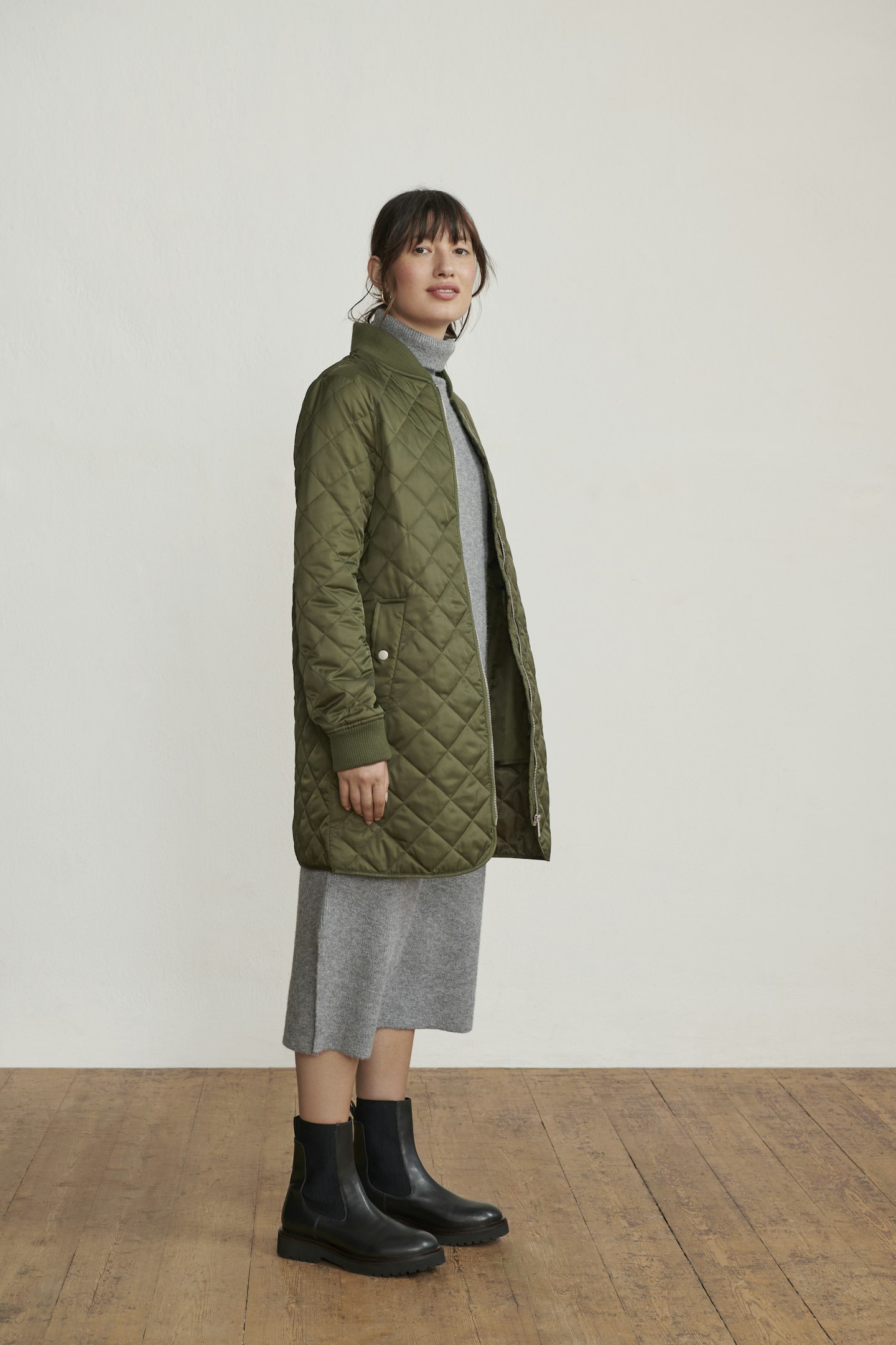 A model wearing a grey sweater dress and green puffer coat 