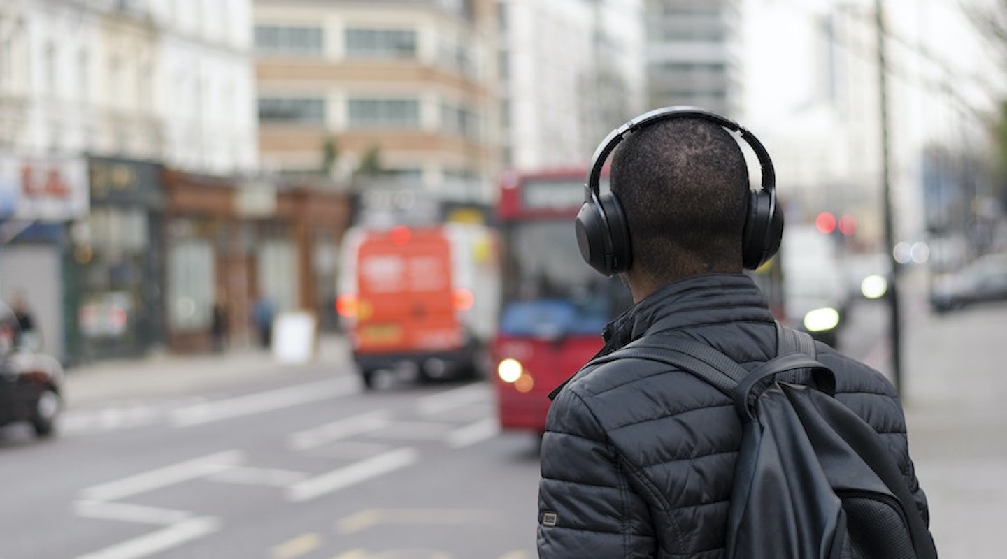 A man wearing headphones while waiting for a bus