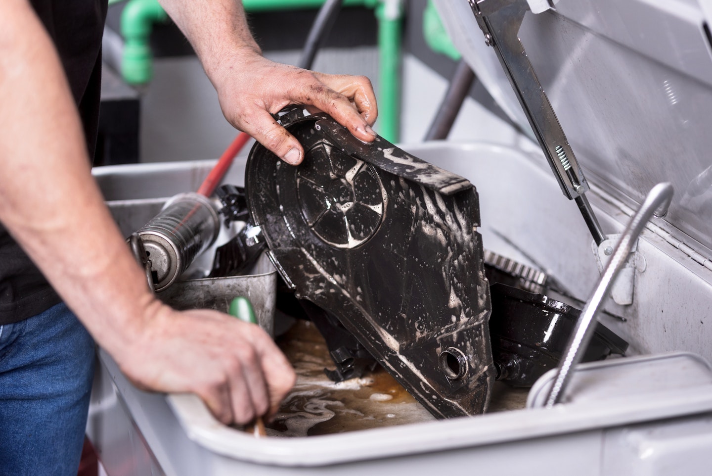 A mechanic degreases an engine part.