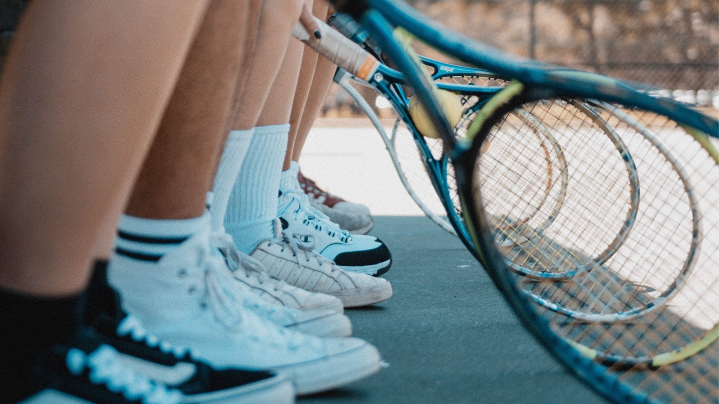 Several different pairs of tennis shoes next to tennis racquets