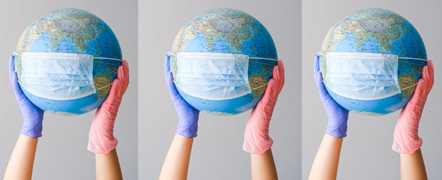 A globe with a mask on it being held up by two hands