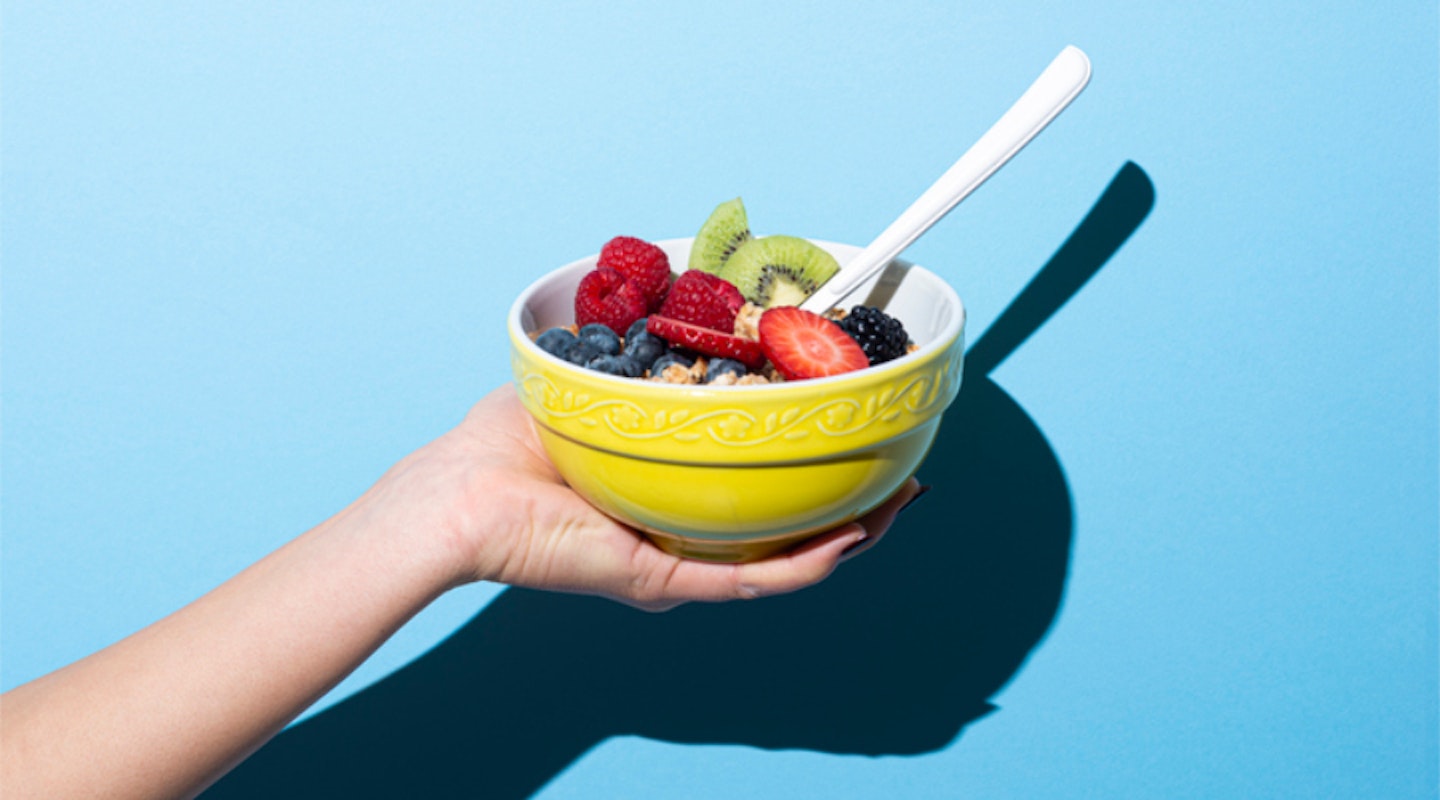 Woman holding a bowl of fruit and granola with vegan yoghurt