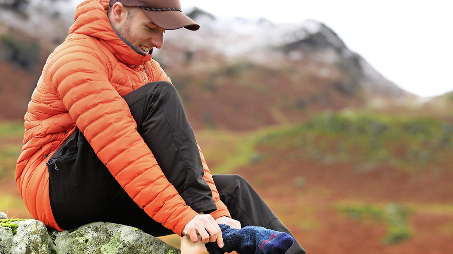 Man putting on walking socks in the mountains wearing a red puffer jacket