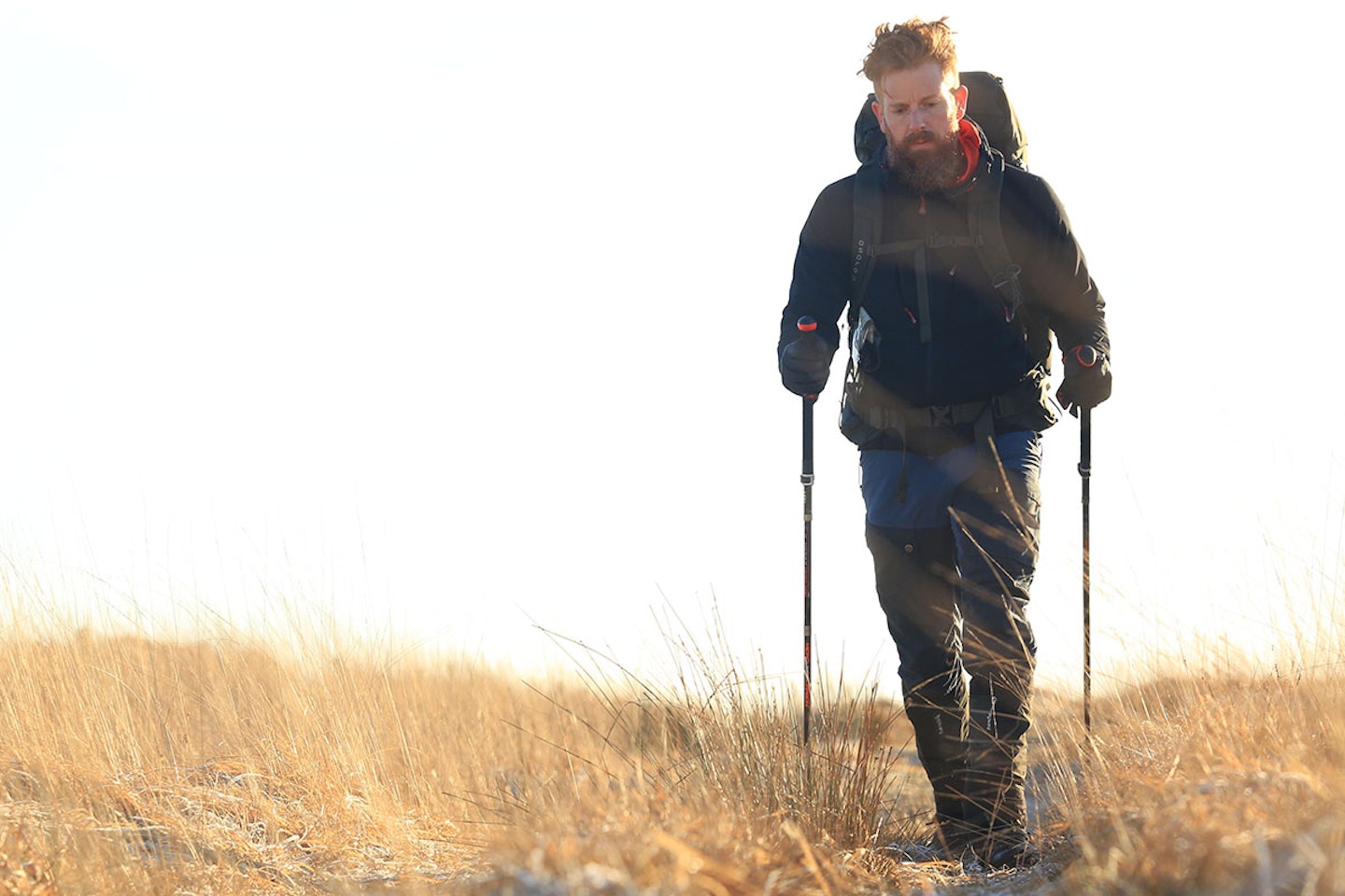 Man in hiking gear walking through grass with trekking poles