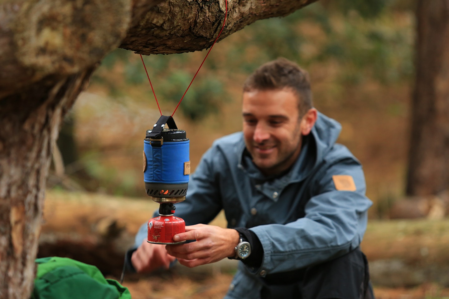Man camping outdoors with backpacking stove hanging from tree