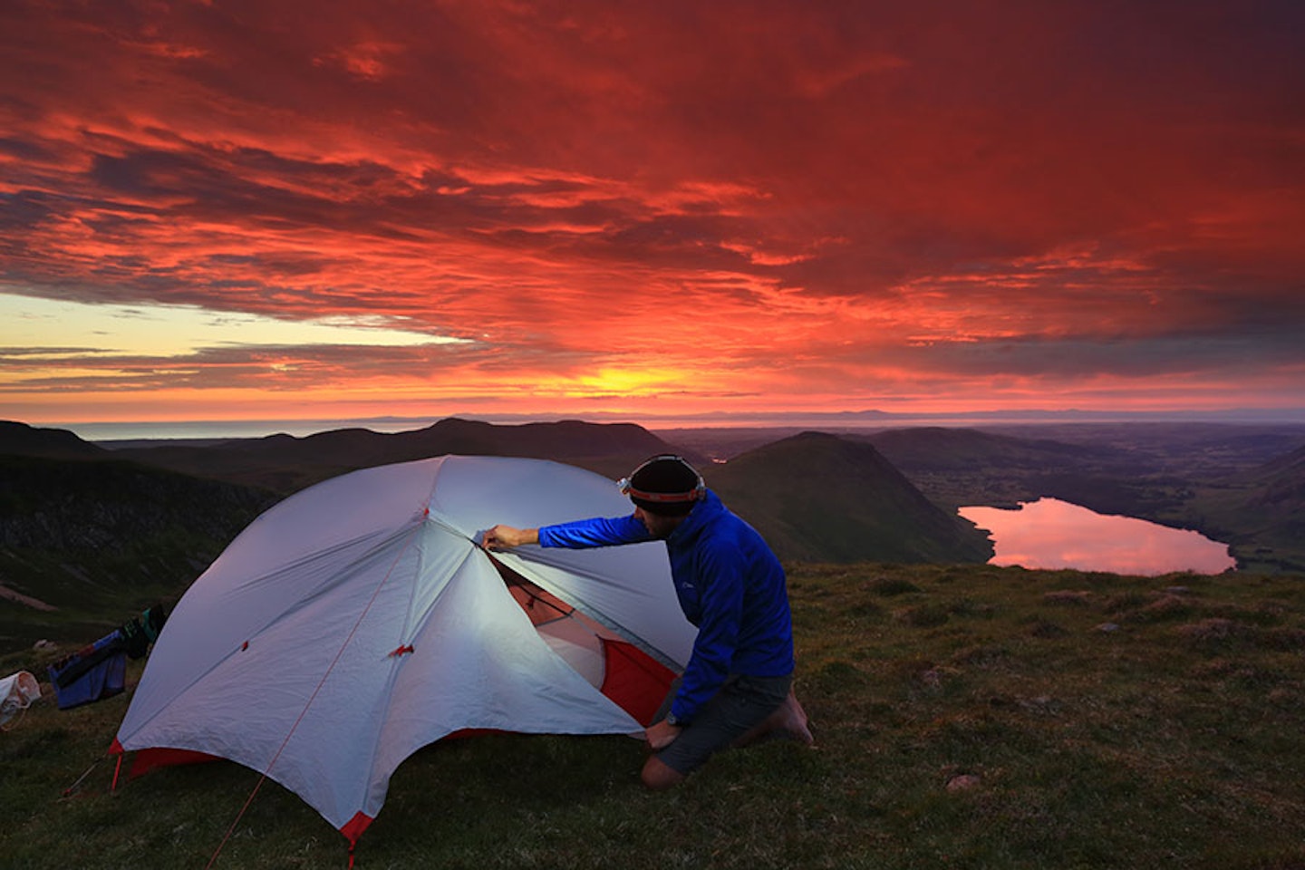 man with head torch lighting up tent at sunset in the mountains 