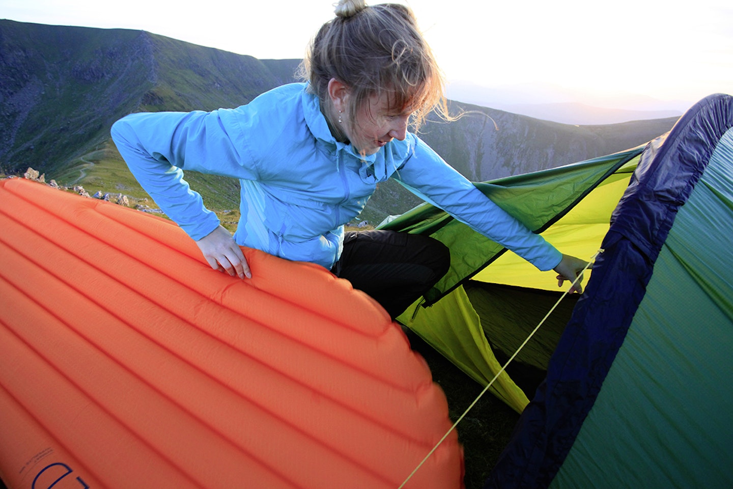 Woman in the mountains putting inflated sleeping mat in tent