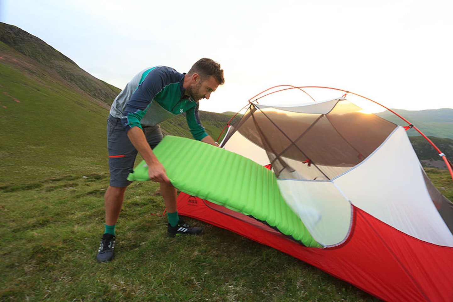 man in shorts putting inflated sleeping mat into a tent in the mountains