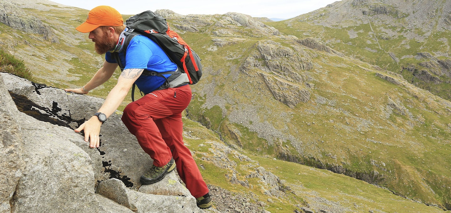 Man scrambling on rocky ridge in red walking trousers