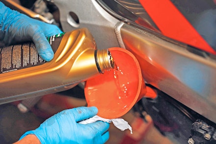 Pouring fresh engine oil into a motorcycle using a funnel