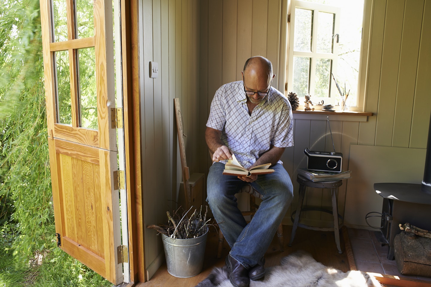 A man sits in a shed listening to a radio while reading 