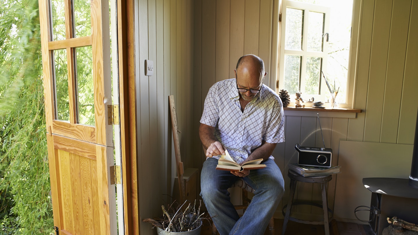 A man sits in a shed listening to a radio while reading 