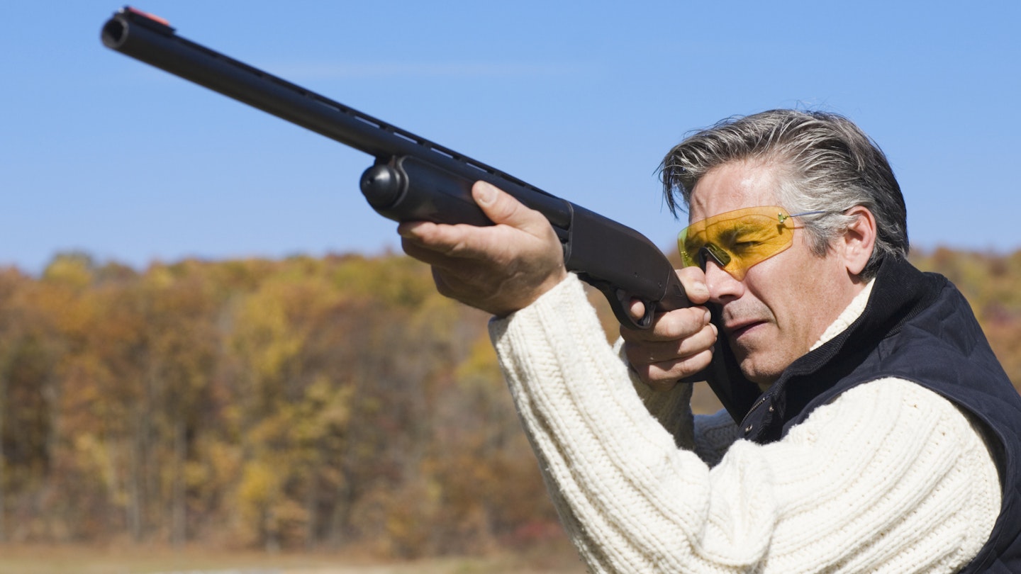 Man wearing hunting glasses aiming a shotgun