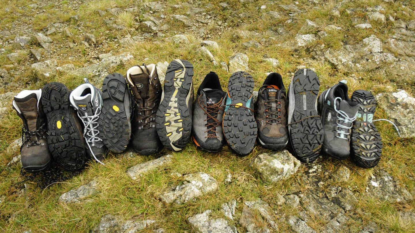 A range of walking boots and shoes lined up on the grass