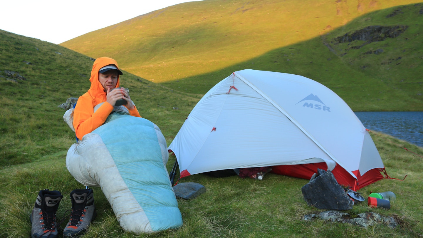 Hiker in sleeping bag at wild campsite in the evening