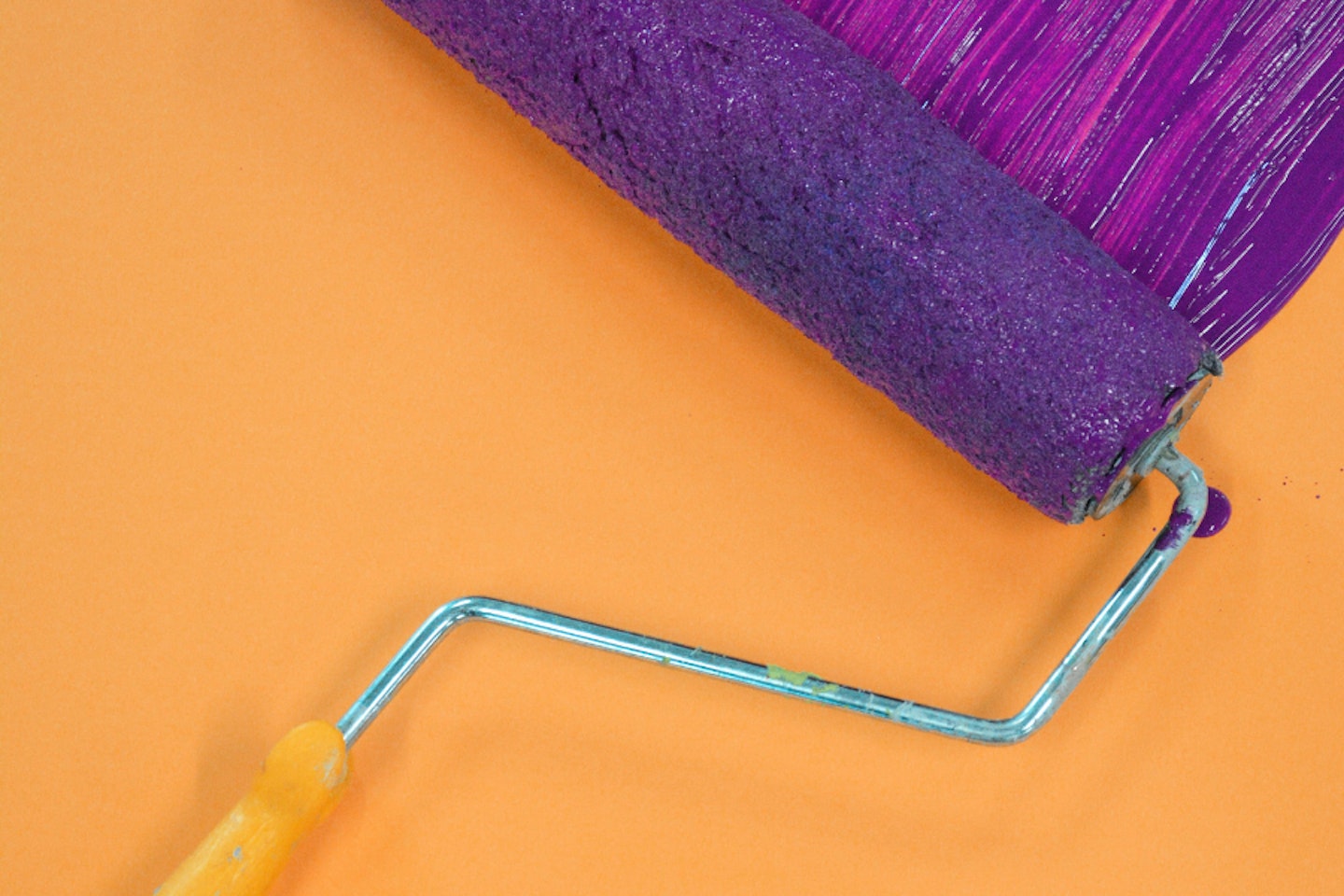 A paint roller with purple paint on a wall