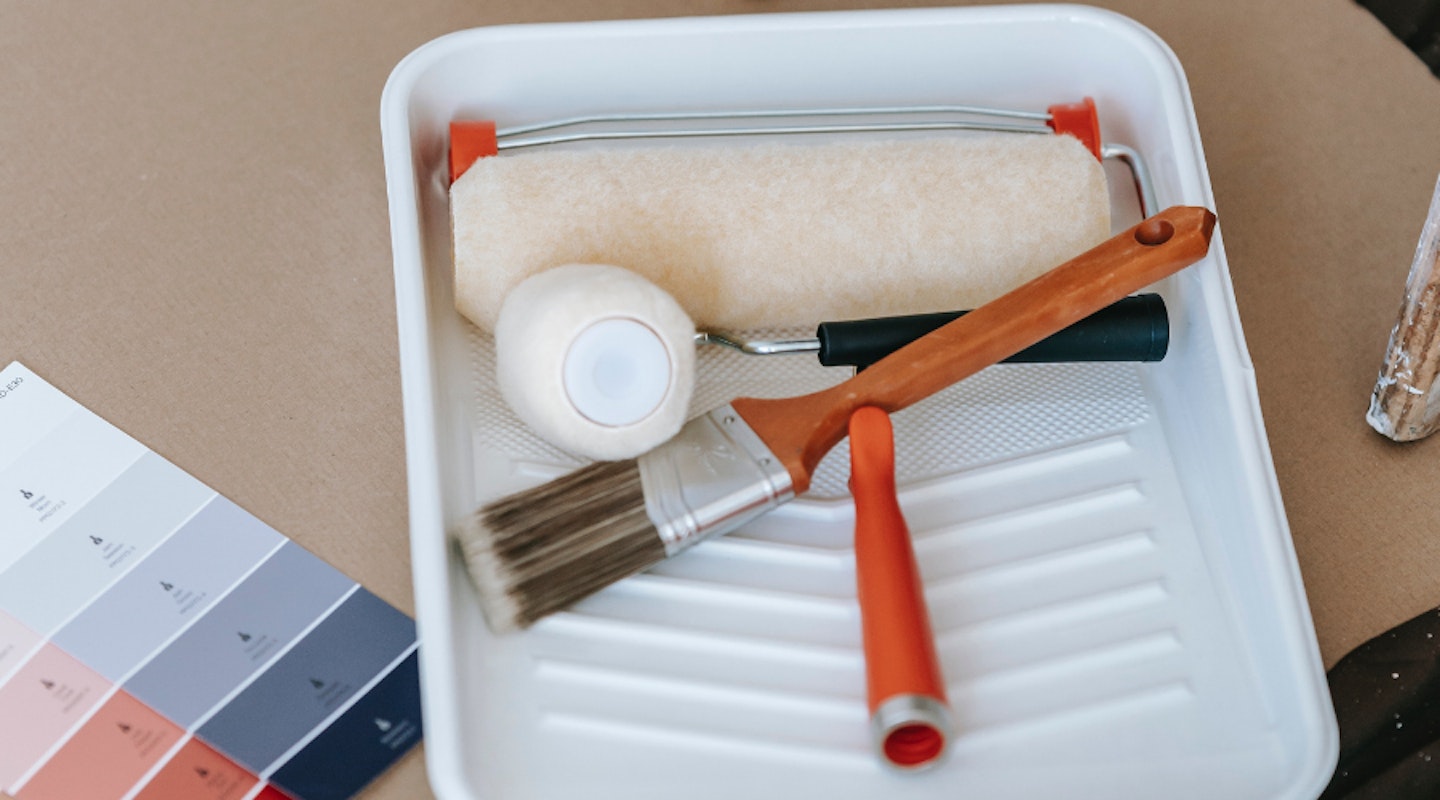 Two paint rollers and a brush in a paint roller tray next to a colour palette swatch