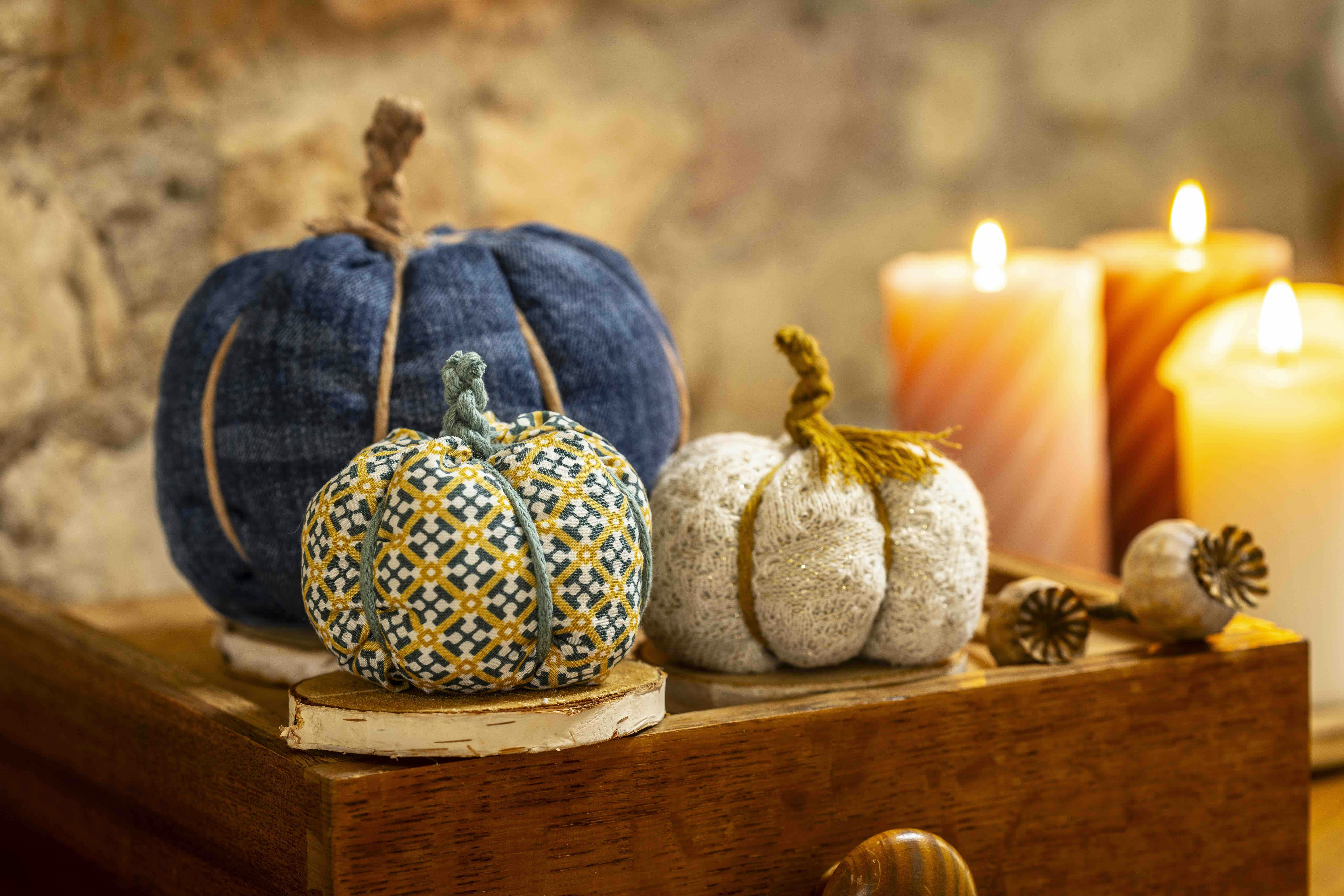 Fabric pumpkins made from recycled clothing, displayed on a rustic table, with flickering candles and poppy seedheads