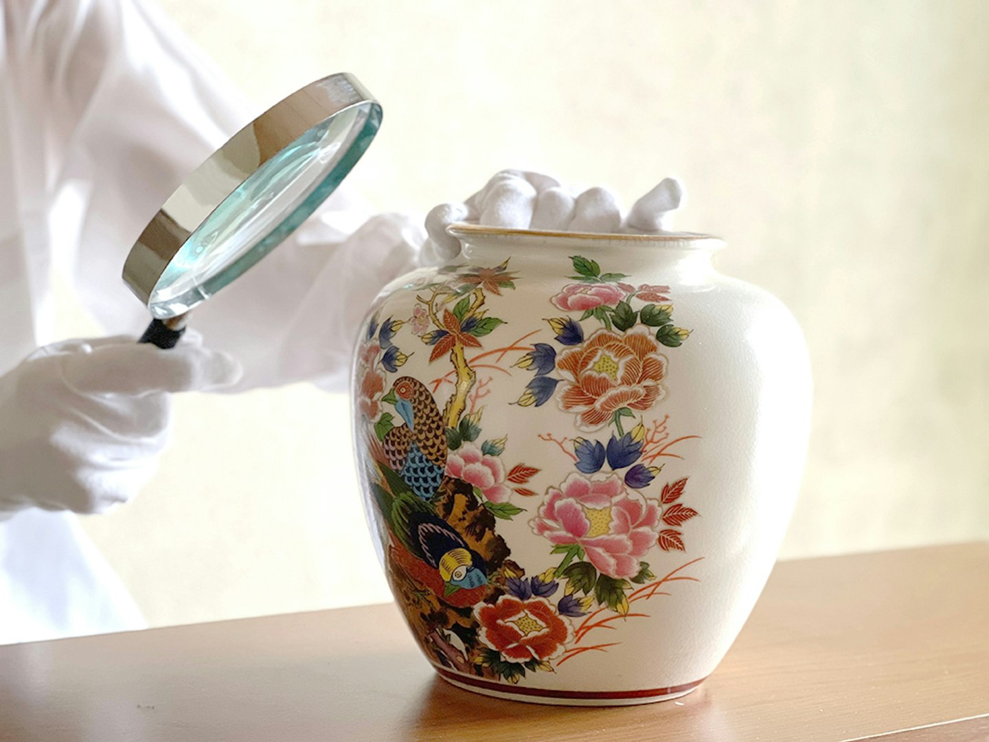 Hands with white gloves to appraise the jar with a magnifying mirror
