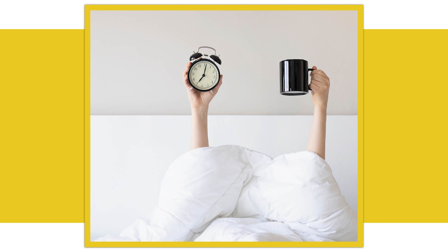 Person in bed under covers holding alarm clock and mug