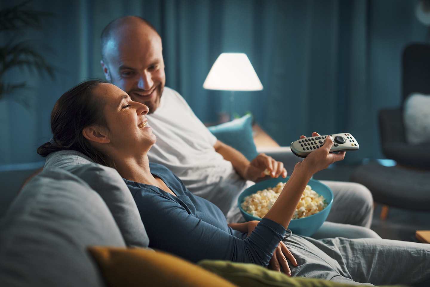 Couple watching film on sofa with popcorn laughing