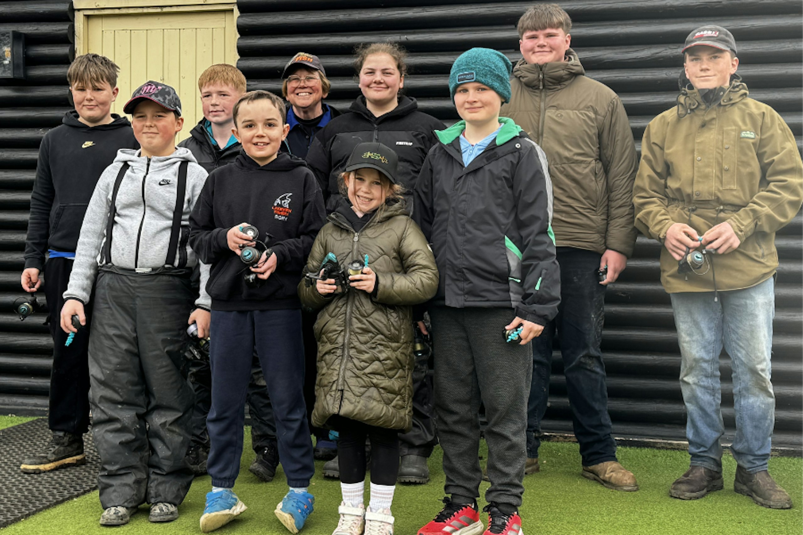 A group of young anglers pose outside a building at Lakeview Fishery, holding fishing reels after a junior match.