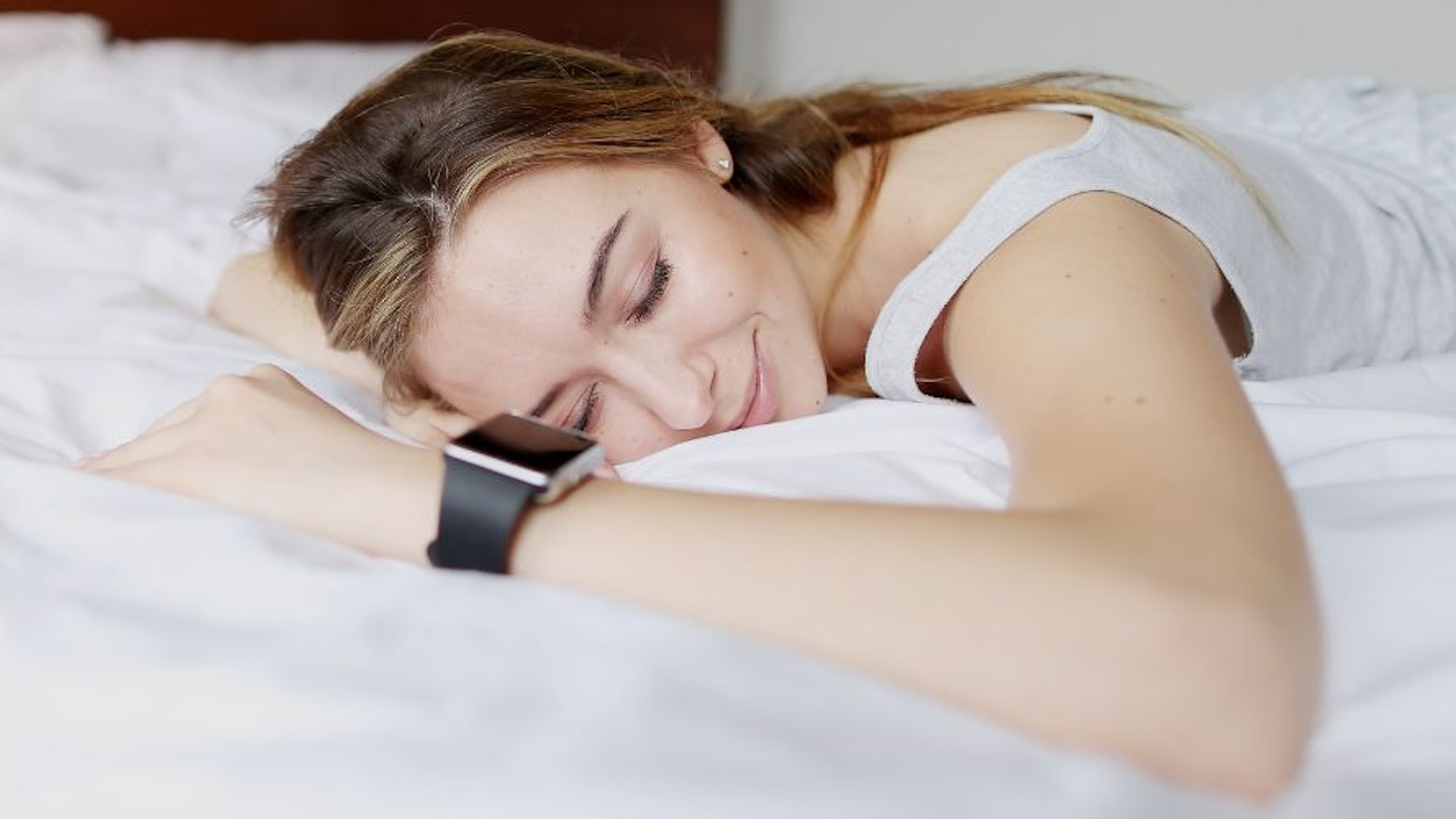 A woman wearing a sleep tracker while asleep on a bed