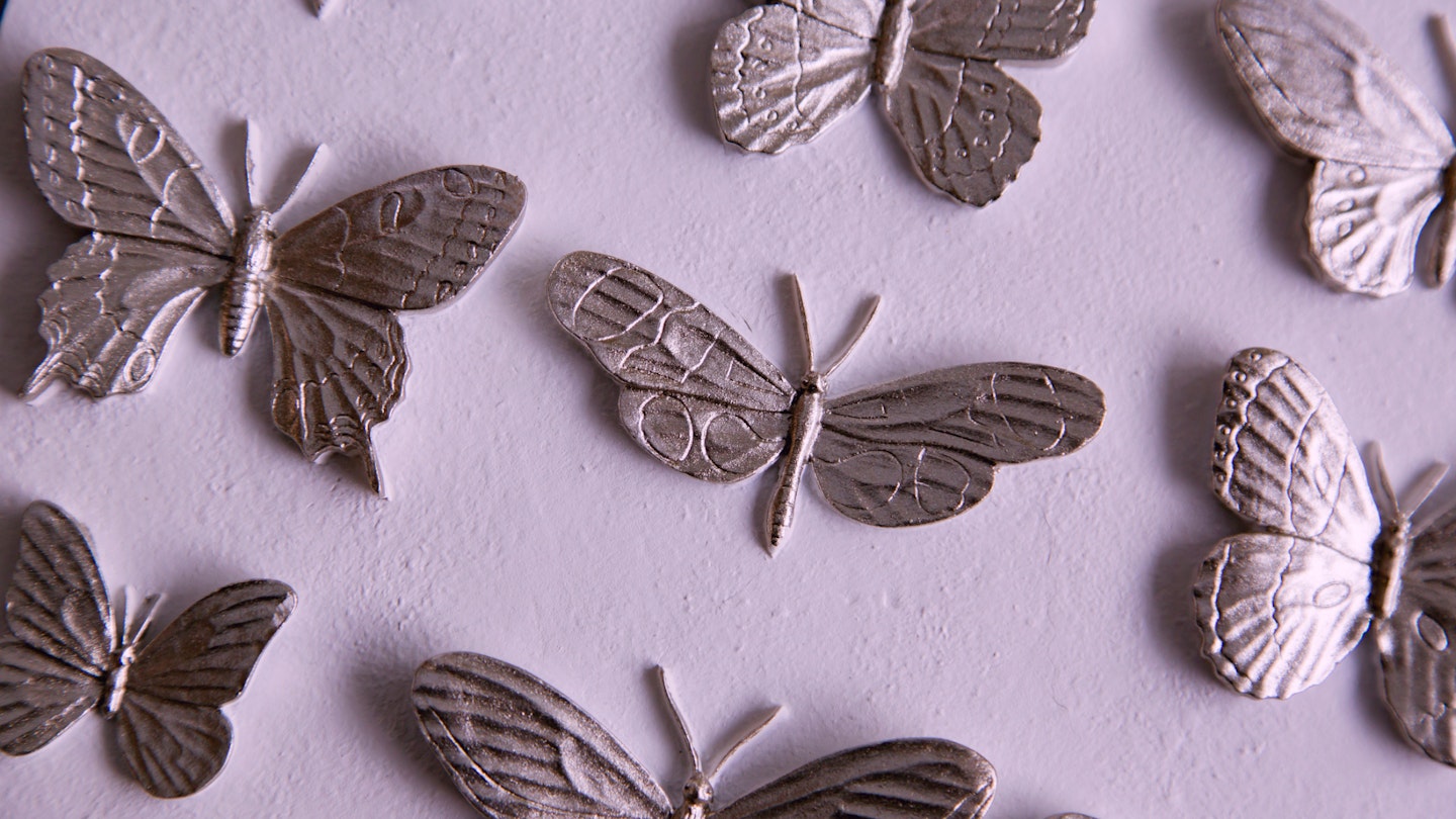 A plaster display of butterflies in metallic pink on a pink background.