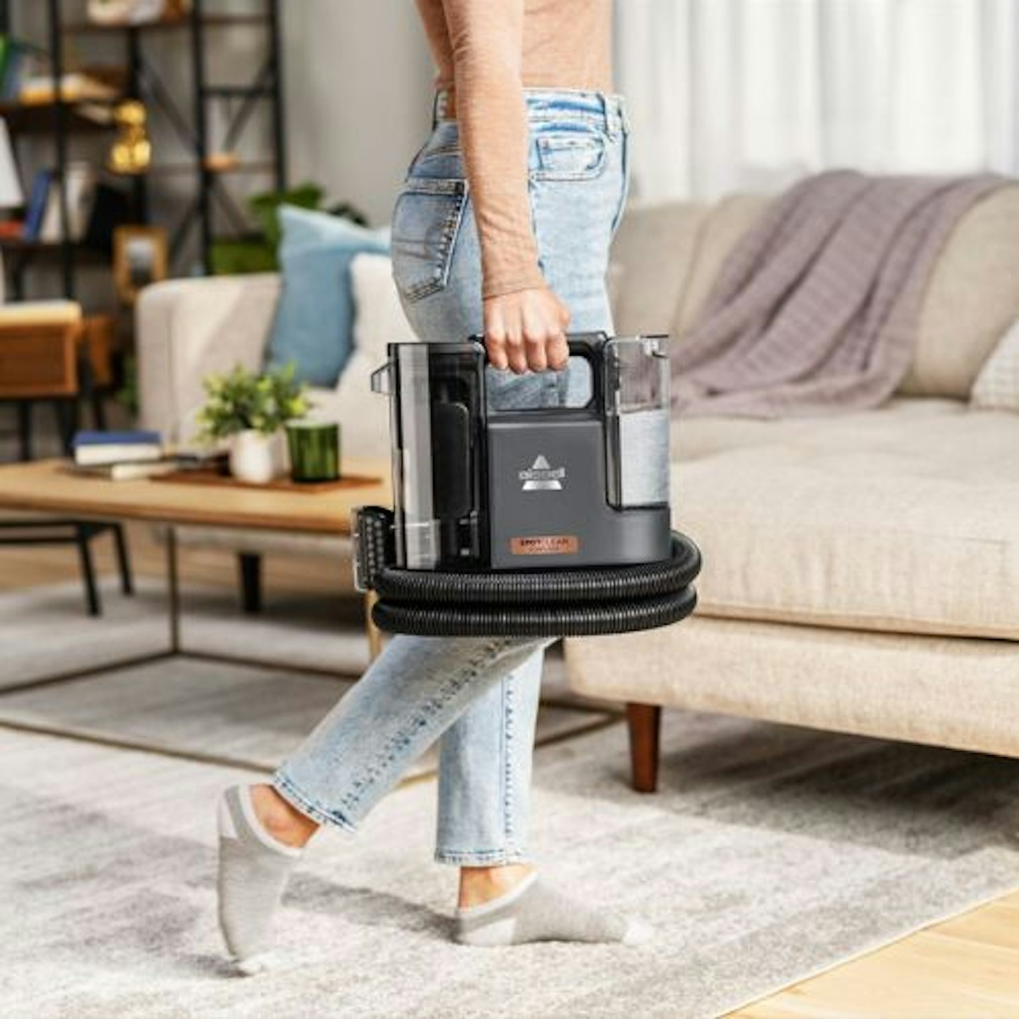 Bissell SpotClean Cordless Spot Carpet Cleaner being carried across a living room by a woman